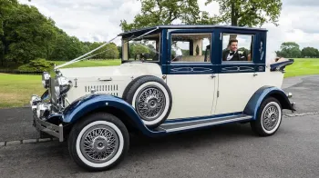 Vintage Imperial in Ivory and Blue with semi-convertible roof open and Bride and Groom seating in the back of the vehicle