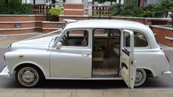 Left side view of classic taxi cab in white with rear passenger door open showing cream leather interior and cream carpet