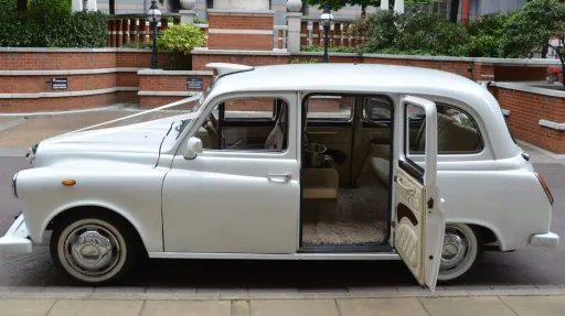 Left side view of classic taxi cab in white with rear passenger door open showing cream leather interior and cream carpet