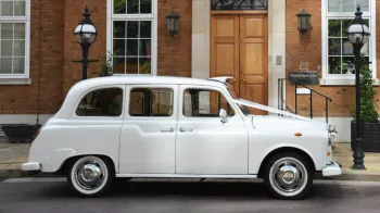 Left side view of a white classic taxi cab with white ribbons accros its bonnet and white wall tires
