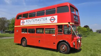 Routemaster London Bus parked on a green field and decorated with white wedding ribbons