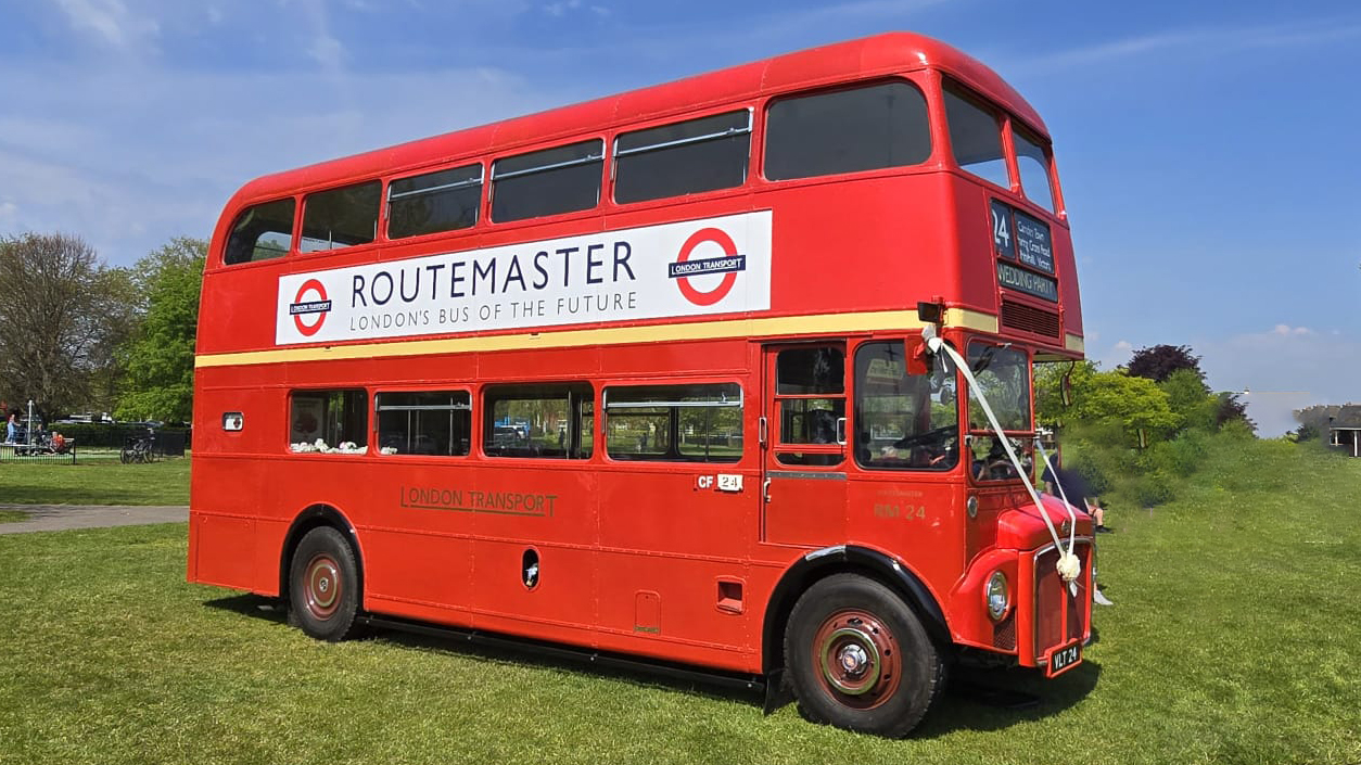 Routemaster London Bus parked on a green field and decorated with white wedding ribbons