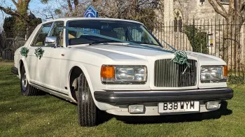 right front view of a classic white Bentley Mulsanne with green ribbons parked in front of a church