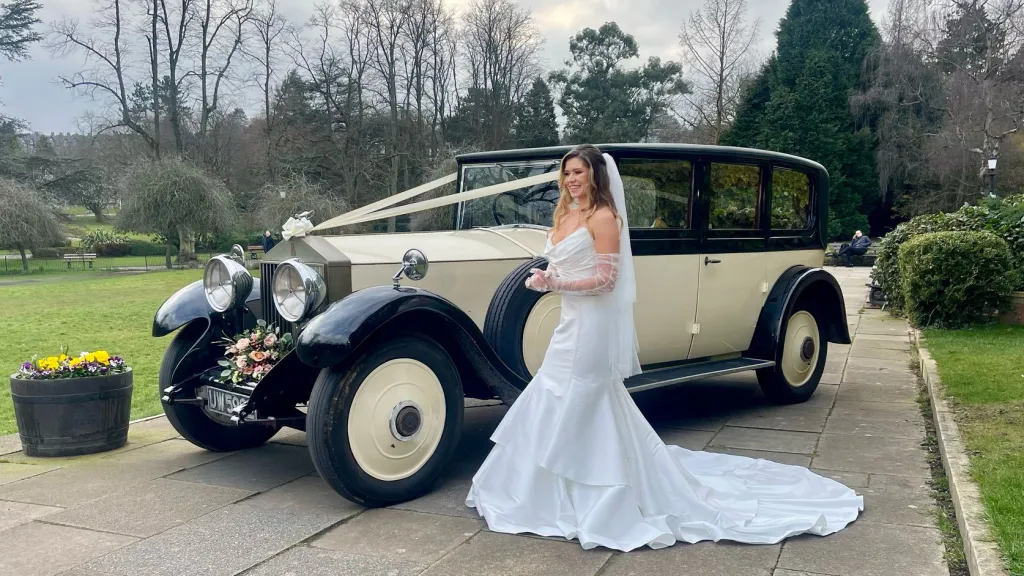 Bride wearing a white wedding dress standing on the left of a Vintage Rolls-Royce in Black and Ivory