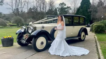 Bride wearing a white wedding dress standing on the left of a Vintage Rolls-Royce in Black and Ivory
