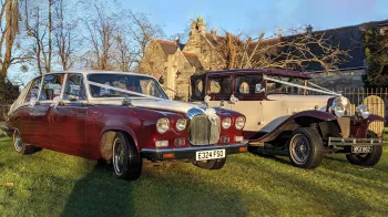 Matching pair of Burgundy and White wedding cars dressed with white ribbons parked in front of a church