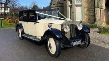 Front side view of Ivory vintage Rolls-Royce with Ivory ribbons on front bonnet, black wheel arches and roof.