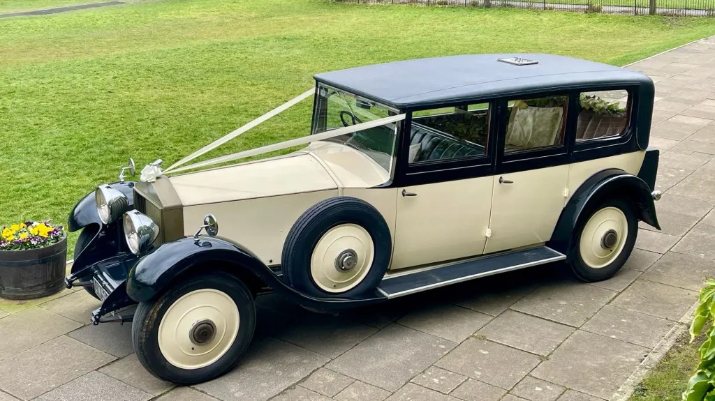 Aerial Left view of 1930s vintage Rolls-Royce Phantom in ivory with black wheel arches and roof. Spare wheel mounted on the left side of the vehicle.