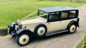 Aerial Left view of 1930s vintage Rolls-Royce Phantom in ivory with black wheel arches and roof. Spare wheel mounted on the left side of the vehicle.