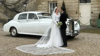 Bride wearing a white wedding dress and Groom in a black suit standing in front of a classic Rolls-Royce Silver Cloud