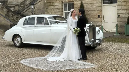 Bride wearing a white wedding dress and Groom in a black suit standing in front of a classic Rolls-Royce Silver Cloud