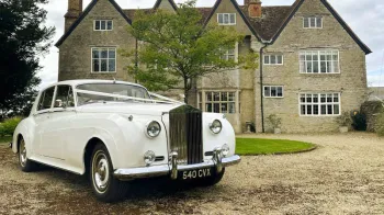 White Classic Rolls-Royce Silver Cloud dressed with wedding ribbons parked in front of wedding venue