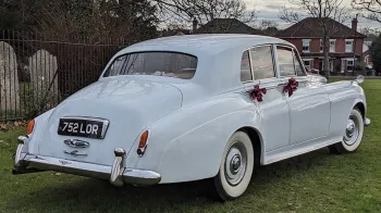 Rear view of a classic Bentley with large white wall tires and Burgundy bows on door handles