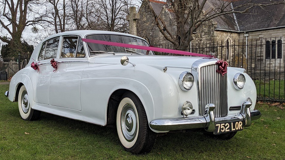 White Classic Bentley is white wall tires and dressed with Burgundy ribbons and bows
