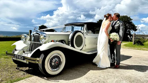 Bride and Groom kissing in front of a Vintage Beauford dressed with ribbons.