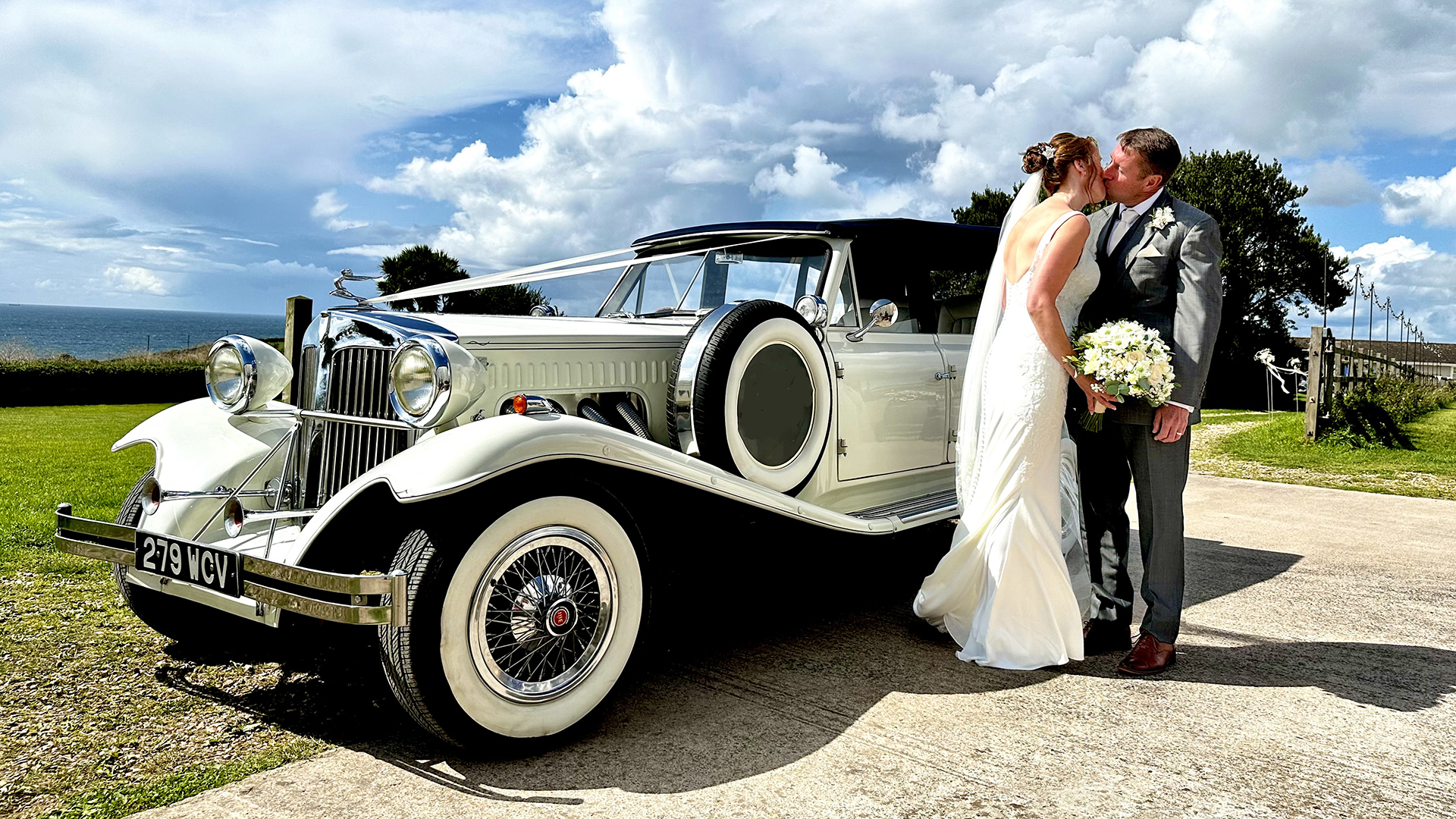 Bride and Groom kissing in front of a Vintage Beauford dressed with ribbons.