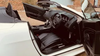 White Aston Martin with convertible roof open and both passenger and driver's doors open showing a black leather interior