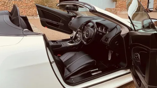 White Aston Martin with convertible roof open and both passenger and driver's doors open showing a black leather interior