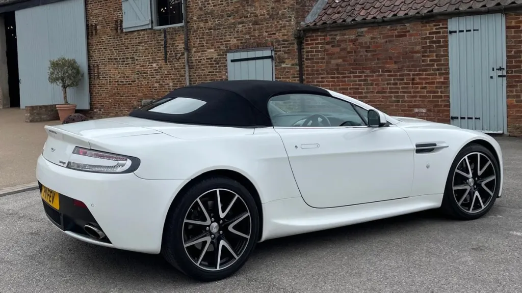 Right side view of white modern Aston Martin Vantage with black soft top roof closed