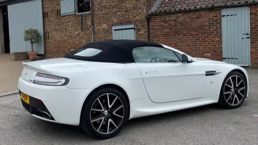 Right side view of white modern Aston Martin Vantage with black soft top roof closed