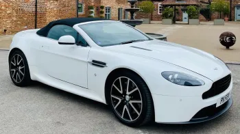 White Aston Martin Vantage Convertible with black soft top roof closed and large chrome black and silver alloy wheels