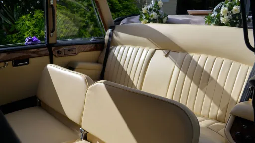 Cream leather interior inside the rear compartment of a classic Daimler Limousine with casual seats raised up.