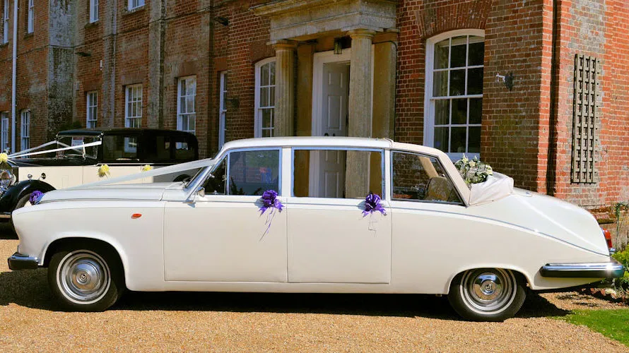 Left side view of classic Daimler Limousine with roof open in Old English White dressed with white ribbons and purple boows on the door handles