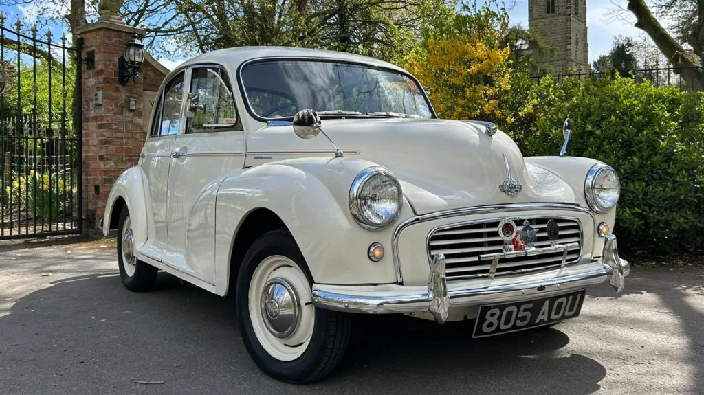 Classic Morris Minor in Old English White poarked in front of a gate of a wedding venue