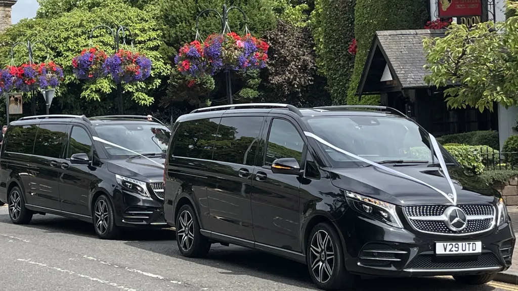 Side view of two identical 7-seater black Mercedes decorated with white ribbons