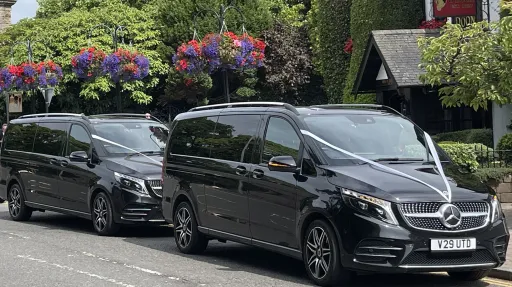 Side view of two identical 7-seater black Mercedes decorated with white ribbons