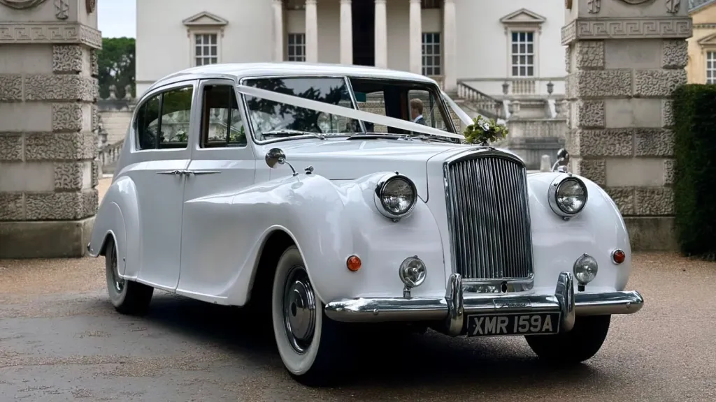 White Austin Princess Limousine with ivory wedding ribbon decoration parked in front of a wedding venue