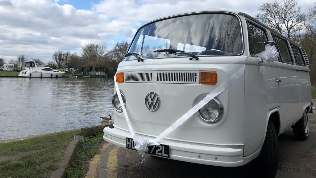 Close-up view of a white classic Volkswagen Campervan with Baywindow decorated with white ribbons and bows on wing mirrors