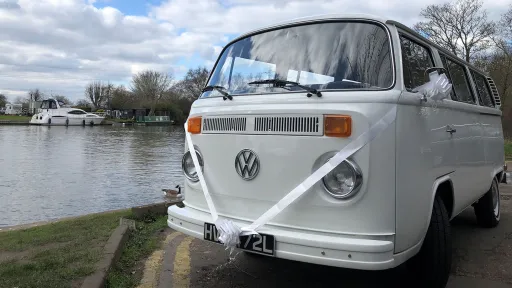 Close-up view of a white classic Volkswagen Campervan with Baywindow decorated with white ribbons and bows on wing mirrors