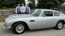 Left side view of a Silver Classic Aston Martin DB6 with Groom and his two groomsmen standing behing the vehicle