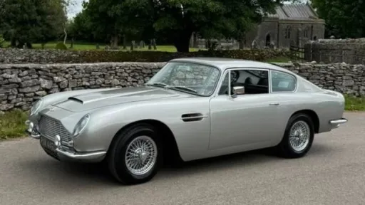 Left side view of Aston Martin DB6 in silver parked in the street. Car has chrome spoke wire wheels.