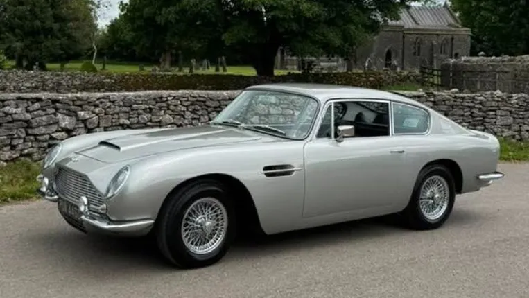 Left side view of Aston Martin DB6 in silver parked in the street. Car has chrome spoke wire wheels.