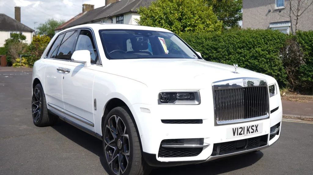 White rolls-Royce Cullinan with large alloy wheels parked in street of London with greenery in the background