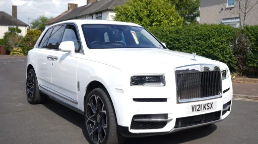 White rolls-Royce Cullinan with large alloy wheels parked in street of London with greenery in the background