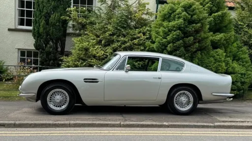 Left side view of silver classic Astion Martin DB6 parked on the siode of the road with greenery in the background