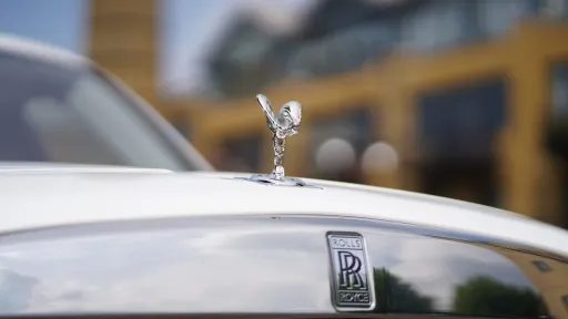 Close up view of Spirit of Ecstasy on top of the bonnet of a White Rolls-Royce Cullinan and the Rolls-Royce badge on top of the chrome front grill