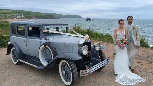 two-tone silver vintage American Buick wedding car with Bride and Groom with Devon coastline in the background