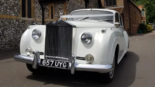 front view of white Classic Rolls-Royce Silver Cloud with Ivory ribbons accros the front bonnet going over the Spirit of Ecstasy, large front chrome grill and chrome bumper