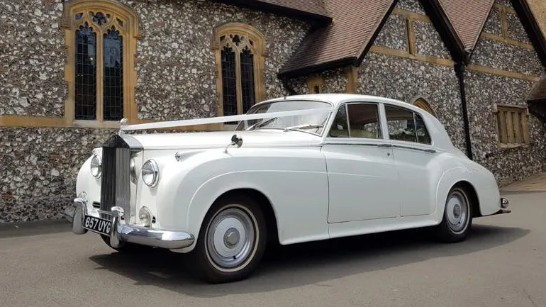 Left side view of white Classic Rolls-Royce Silver Cloud  with wedding ribbons accros its front bonnet parked in front of a church in London