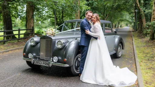 Bride and Groom holding each others and standing next to a vintage Royale Windsor with convertible roof open