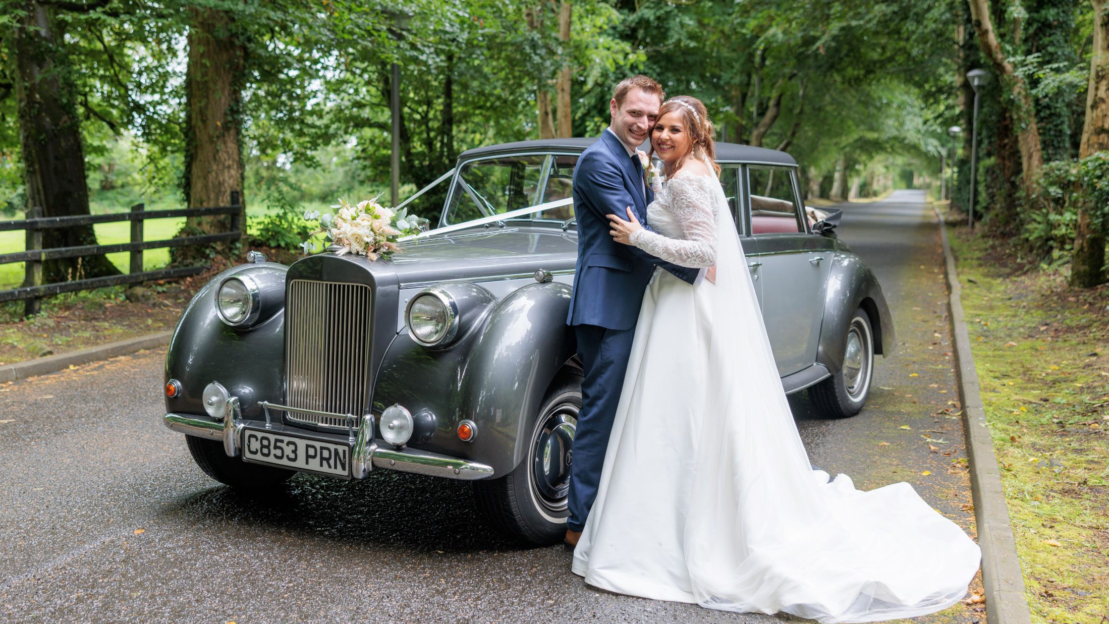 Bride and Groom holding each others and standing next to a vintage Royale Windsor with convertible roof open