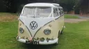 Front view Classic Volkswagen Campervan in White & Cream with garland of pink flowers on front bumper and light pink ribbons accros the front of its bonnet