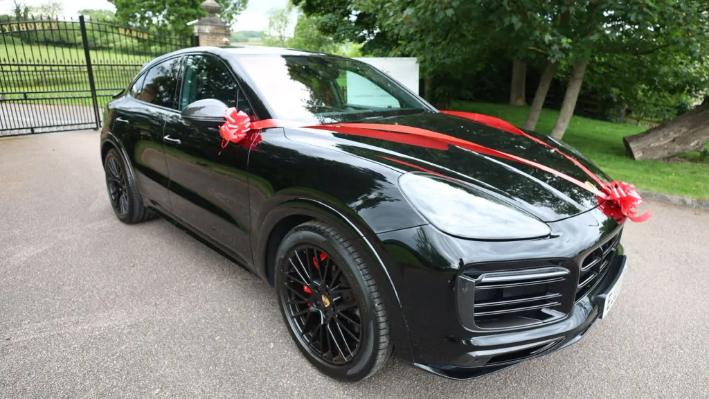 Black Porsche Cayenne GTS right side view with large black alloy wheels and red Ribbons and Bows across the front bonnet