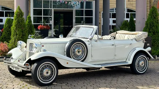 White Vintage-style Beauford with Convertible roof down, thin white wall tires and spare wheel mounted in the side of the vehicle