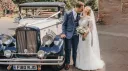 Bride and groom kissing and standing next to a vintage-style regent in white with black wheel arches.