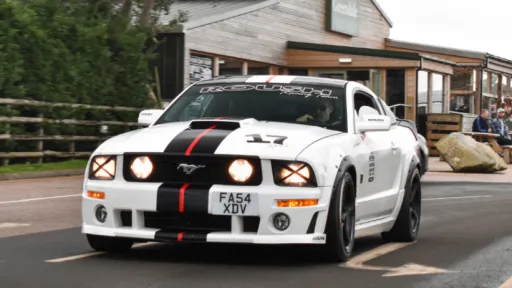 White Mustang GT v8 with black stripes in street with headlights on